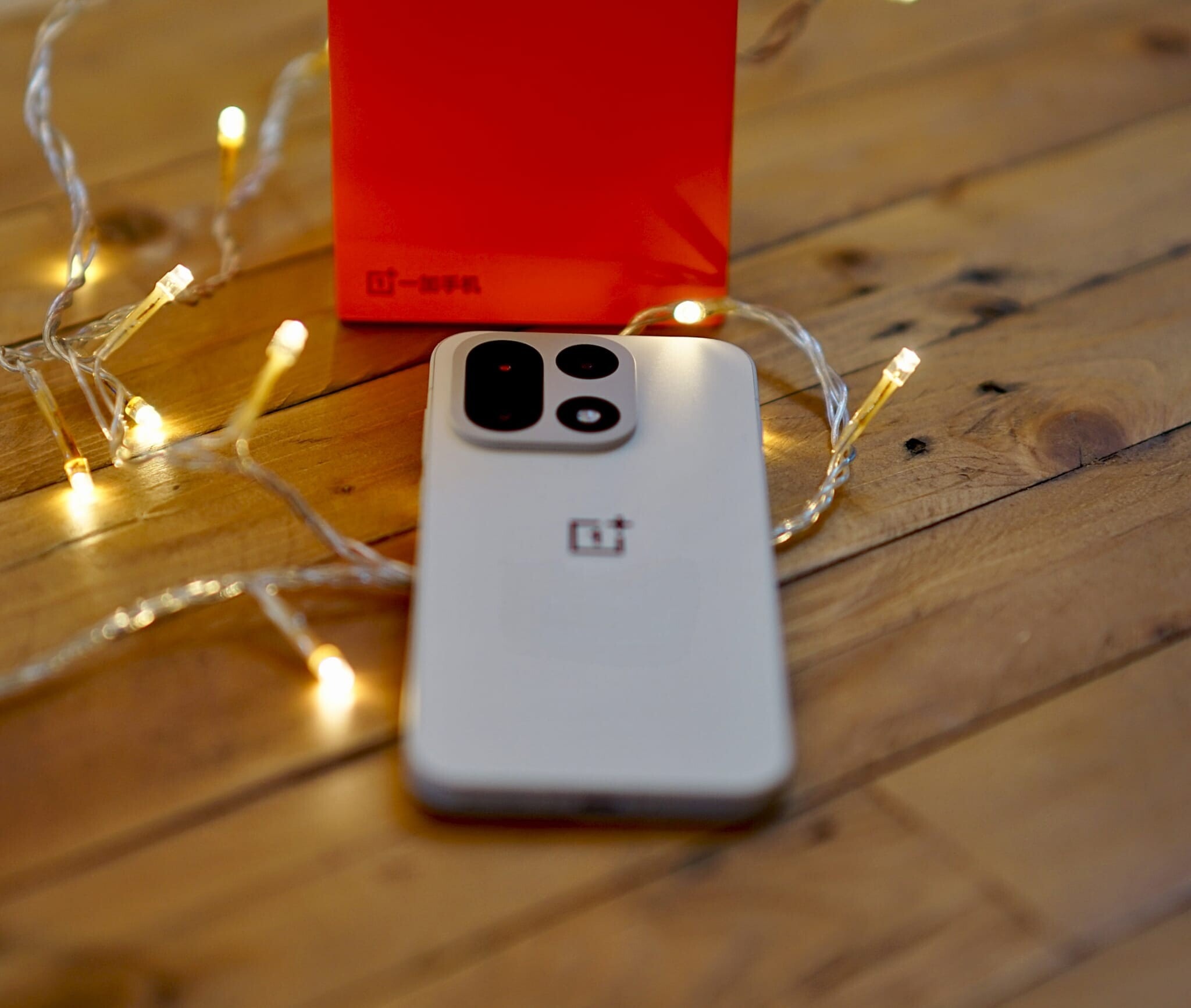 Một chiếc điện thoại OnePlus 15 đặt trên bàn gỗ cạnh hộp đựng sản phẩm màu đỏ đặc trưng.