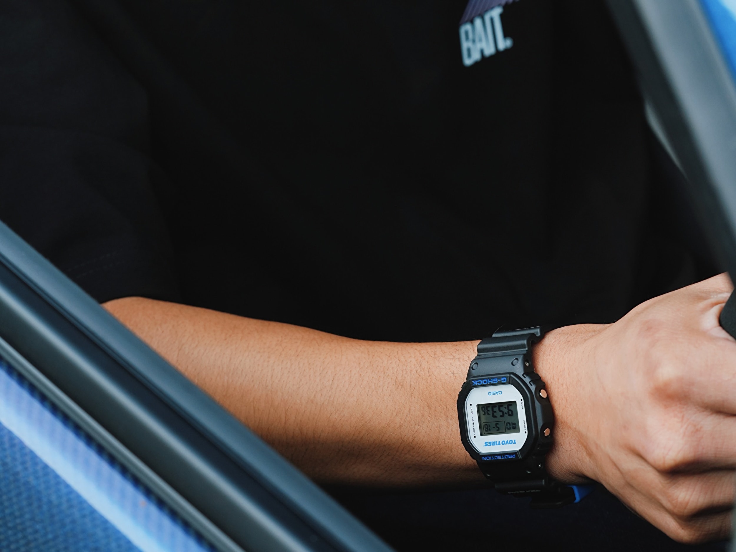 Người đeo đồng hồ Casio G-Shock DW5600TT25-1 x Toyo Tires ngồi trong xe hơi.
