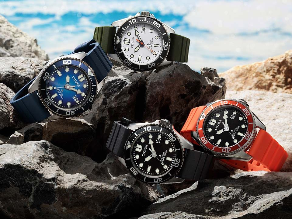 Bốn mẫu đồng hồ lặn Citizen Promaster Marine với các màu trắng, đen, xanh dương và cam hiển thị trên đá ven biển.